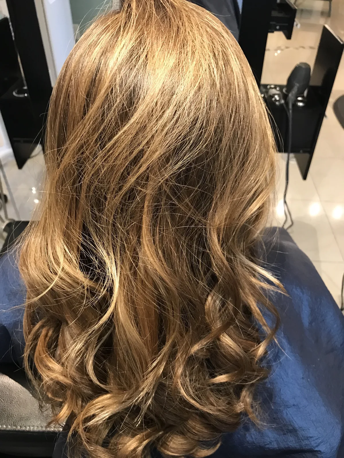 Deva cut with golden-blonde balayage on long waves, back view by Richie at Damron & Company Salon in Austin