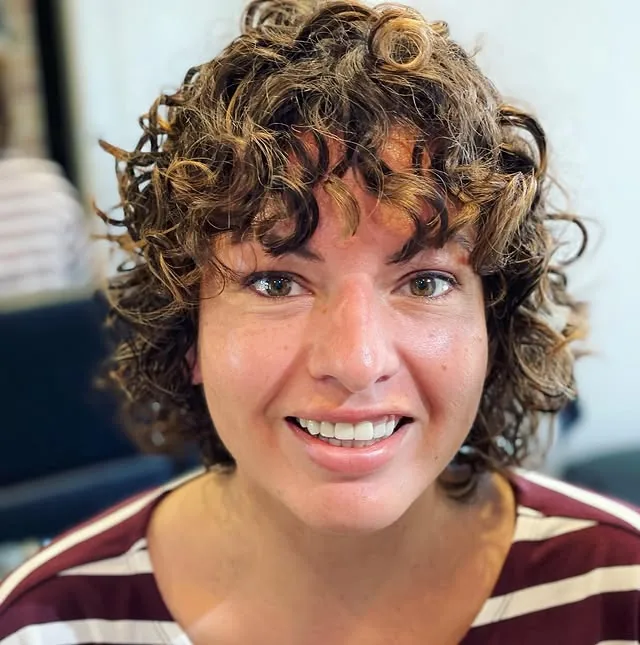Deva cut with caramel highlights on a short curly shag with curly bangs, smiling client by Richie at Damron & Company Salon in Austin