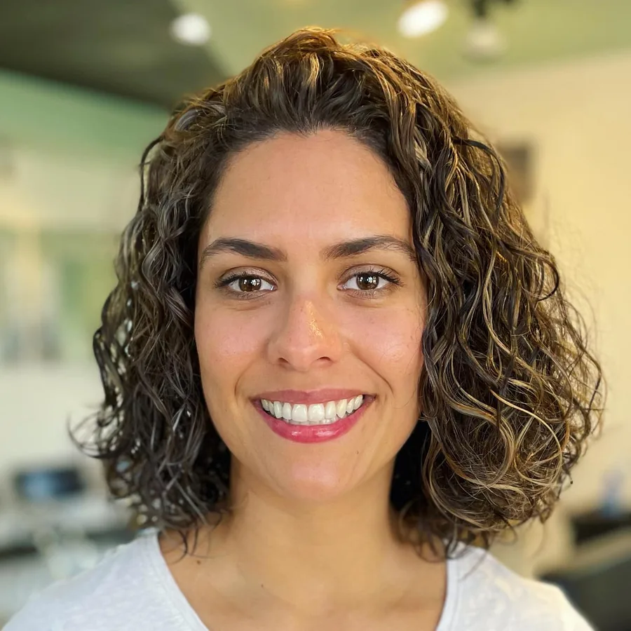 Deva cut with blonde highlights on shoulder-length loose curls, smiling client by Richie at Damron & Company Salon in Austin