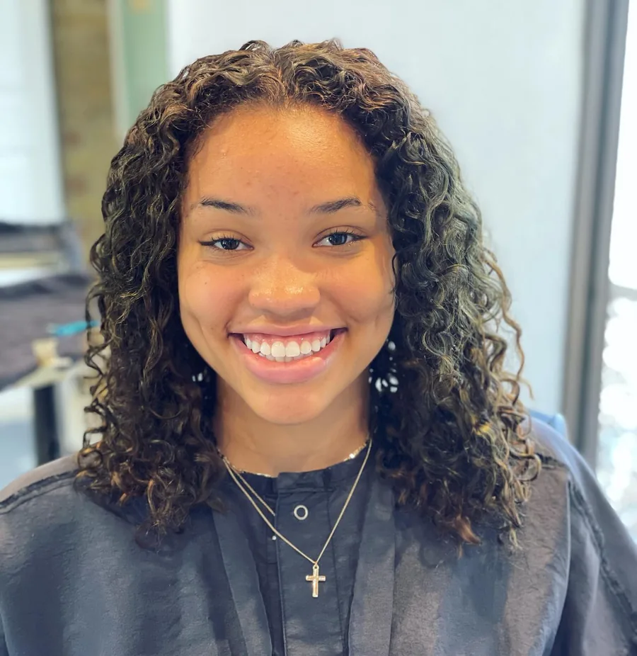 Deva cut with subtle highlights on shoulder-length tight ringlets, smiling client by Richie at Damron & Company Salon in Austin