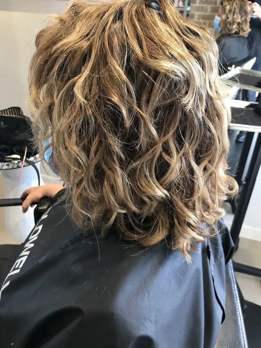Deva cut with blonde highlights on shoulder-length waves, back view by Richie at Damron & Company Salon in Austin