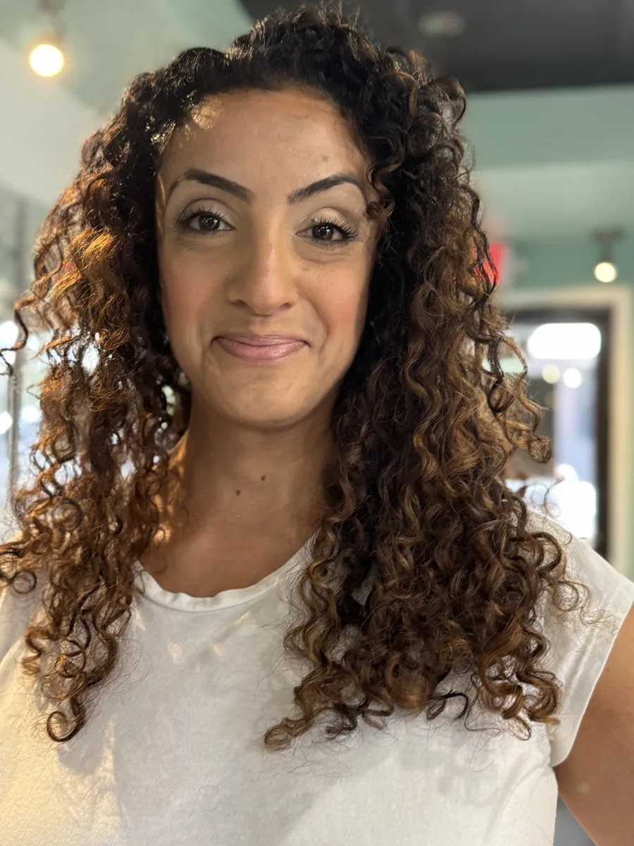 Deva cut and color on long tight ringlet curls with caramel tones, smiling client by Richie at Damron & Company Salon in Austin