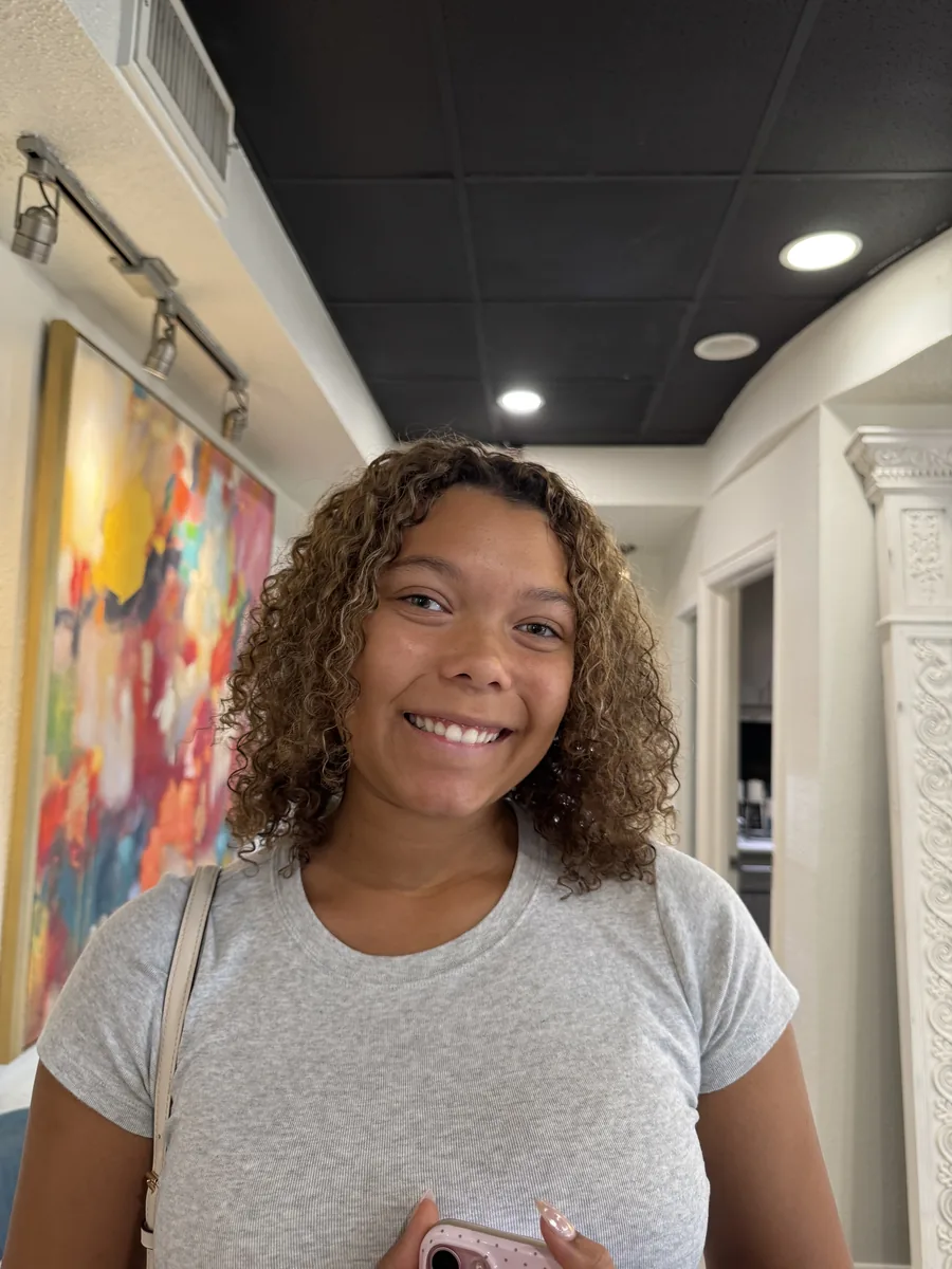 Deva cut on shoulder-length golden-brown ringlets, smiling client by Richie at Damron & Company Salon in Austin