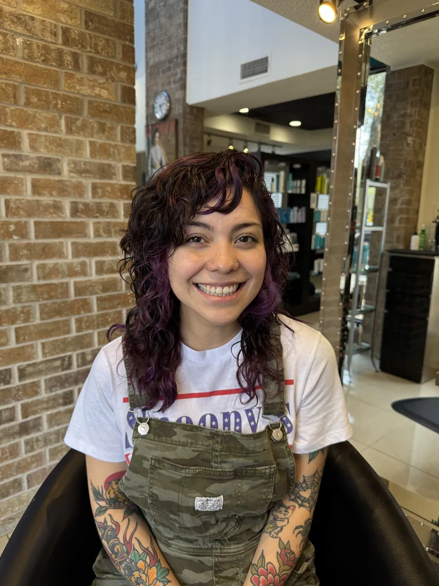Deva cut curly shag with purple tones and curly bangs, smiling client by Richie at Damron & Company Salon in Austin