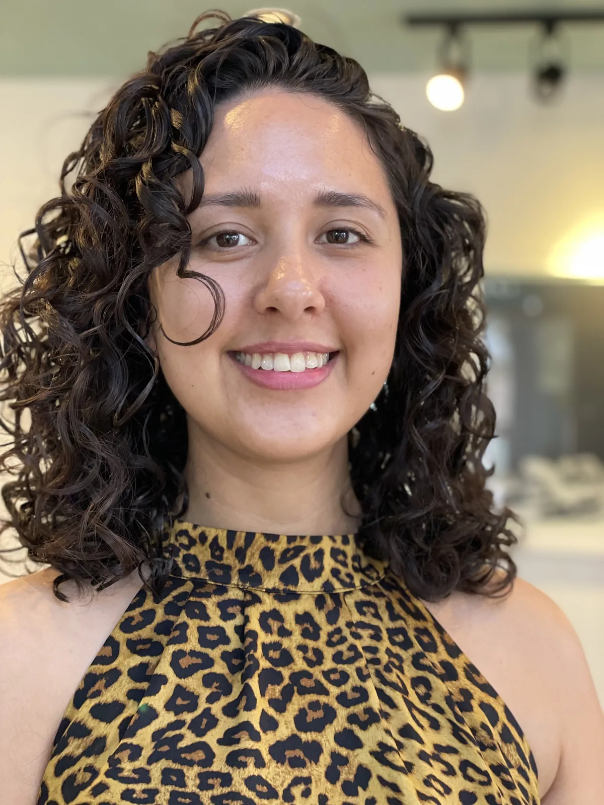 Deva cut on shoulder-length dark-brown springy curls with a face-framing ringlet, smiling client by Richie at Damron & Company Salon in Austin