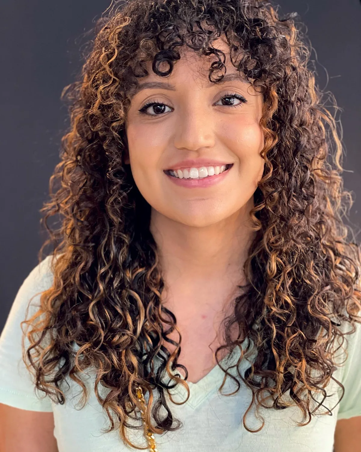 Rëzo cut with balayage on long dark ringlet curls with caramel highlights and curly bangs by Richie at Damron & Company Salon in Austin